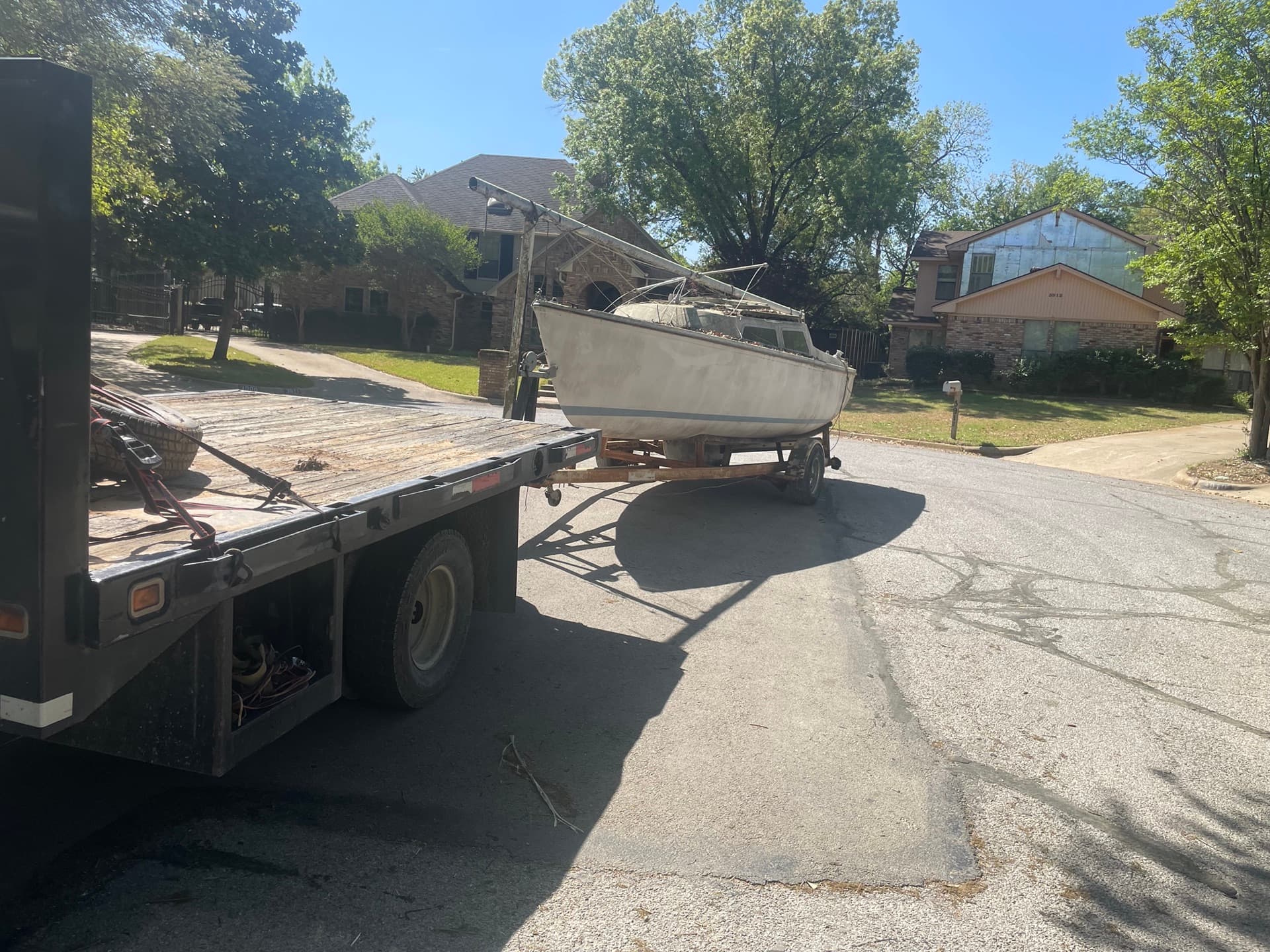 Small sailboat on a trailer being moved to a flatbed truck on a residential street